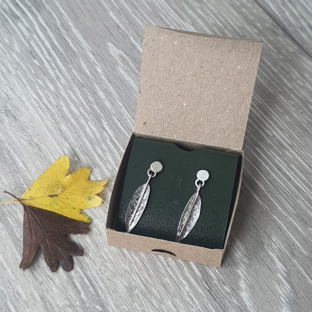 A pair of silver leaf earrings in a card box.
